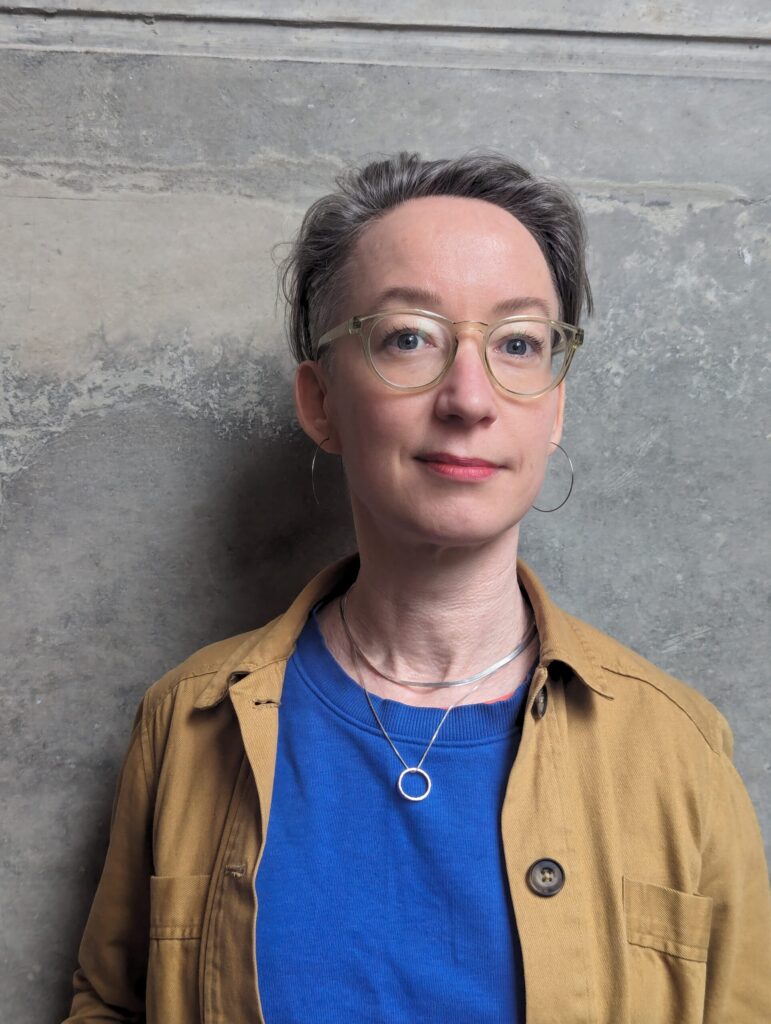 a picture of jo, they are a white person in their mid forties wearing glasses, with short hair and smiling a bit